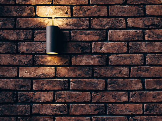 lighting options for home décor - black round wall sconce lit against a red brick wall